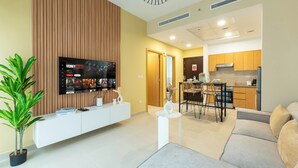 A modern living area with a flat-screen TV, a dining table, and a kitchen in the background. - Downtown Dubai - Pool & Gym Access (Dubai)