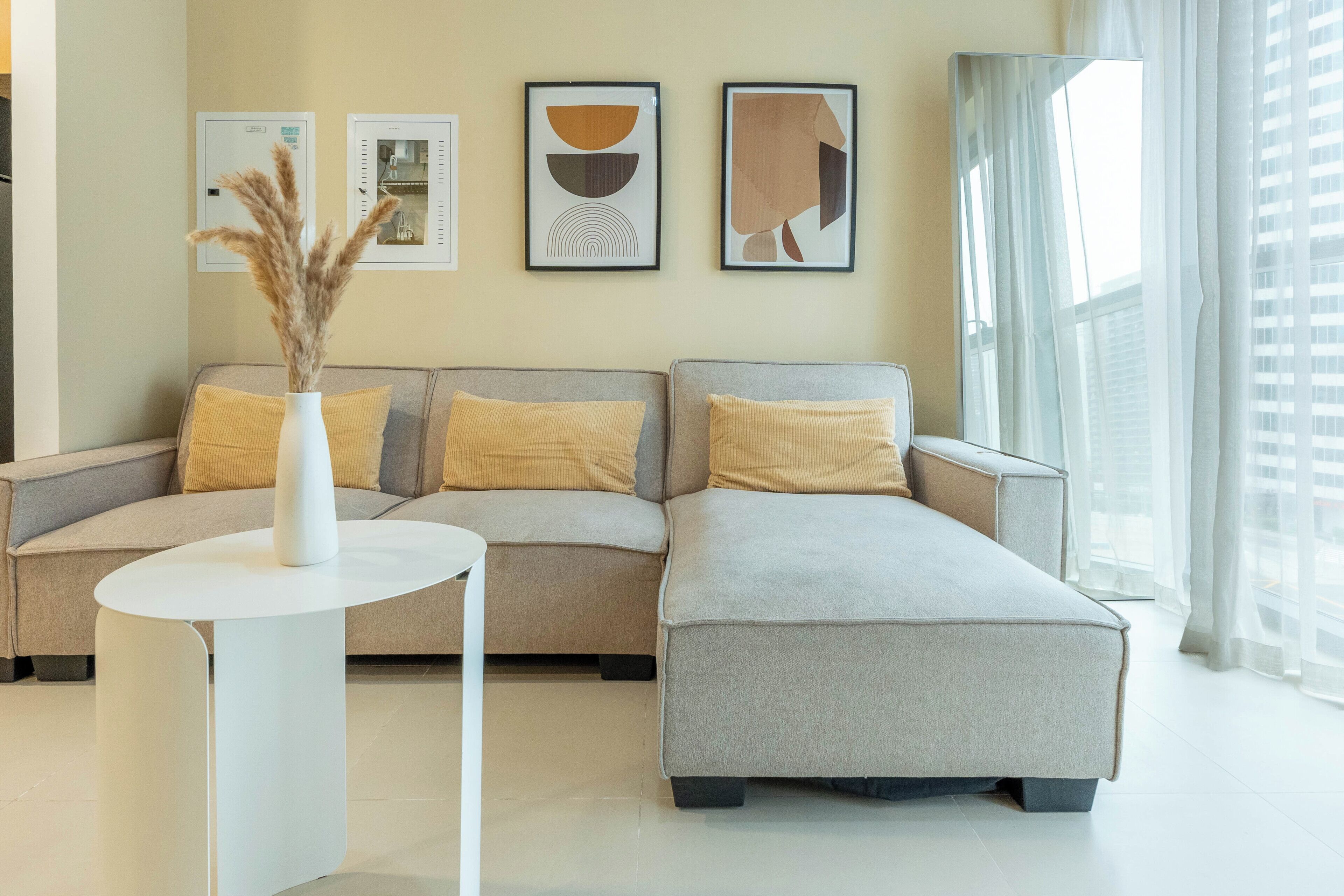 A modern living room with a grey sectional sofa, a white round table, and three framed abstract artworks on the wall.