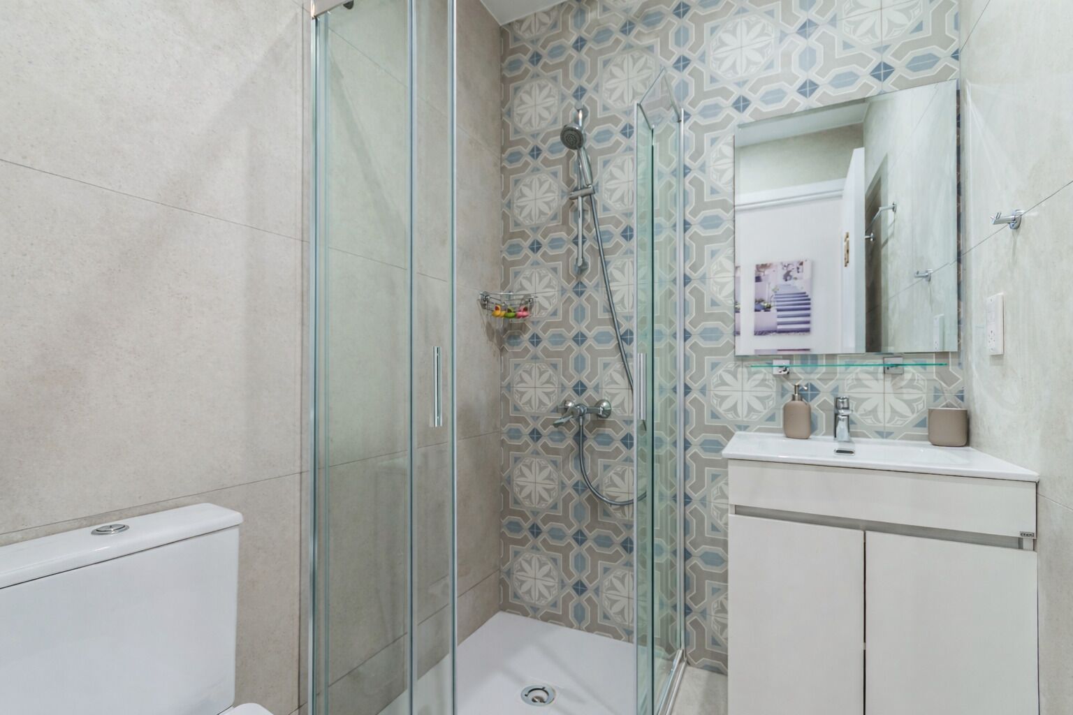 Een badkamer met een douchecabine van glas, een wit wastafeltje en een wand met een patroon.