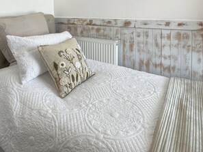 A bed with a quilted headboard, a radiator, and a wooden wall paneling.