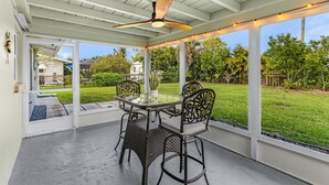 A covered patio with a table and chairs, a ceiling fan, and a view of a green lawn and trees. - 5 min to Beach - Newly Renovated (Cape Coral)