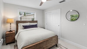 A bedroom with a bed, a ceiling fan, a nightstand, a lamp, a window, and a door. - 5 min to Beach - Newly Renovated (Cape Coral)