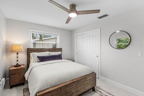 Ein Schlafzimmer mit Bett, Deckenventilator, Nachttisch, Lampe, Fenster und Tür.