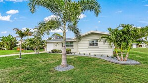 A residential house with a well-maintained lawn, palm trees, and a clear sky. - 5 min to Beach - Newly Renovated (Cape Coral)