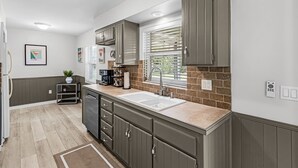 A kitchen with a double sink, dark cabinets, a window with blinds, and a small shelf with a plant. - 5 min to Beach - Newly Renovated (Cape Coral)