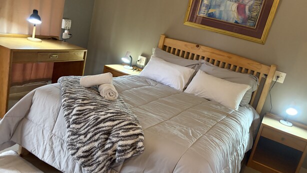 A neatly made bed with a striped blanket and rolled towel, a bedside lamp, a nightstand with a phone, and a framed picture on the wall. - Perfect 3 x 1-bedroom Rooms in beautiful Sasolburg for your getaway (Sasolburg)