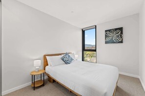 A bedroom with a bed, a nightstand, a lamp, a window with a view, and a wall art piece.