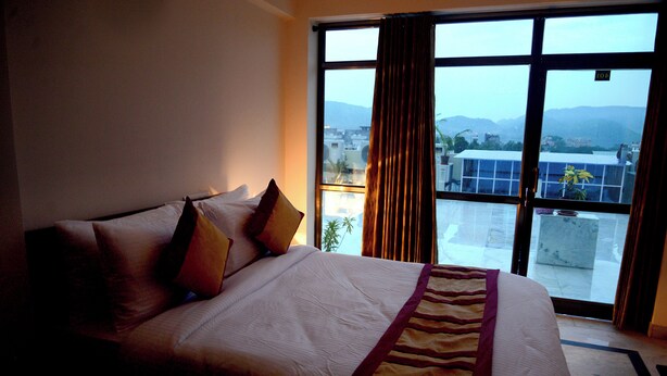 Ein Hotelzimmer mit einem großen Bett, Blick auf die Stadt durch ein Fenster und ein Balkon mit Bergblick.