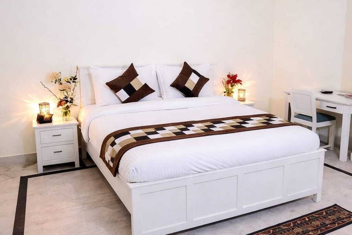 Quarto com cama, mesas de cabeceira, escrivaninha e aparelho de ar condicionado.