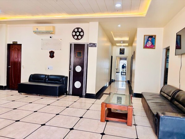 A hotel lobby with a black leather sofa, a glass coffee table, a clock, and a door with a sign. - Hotel Roselle Heights (Jaipur)