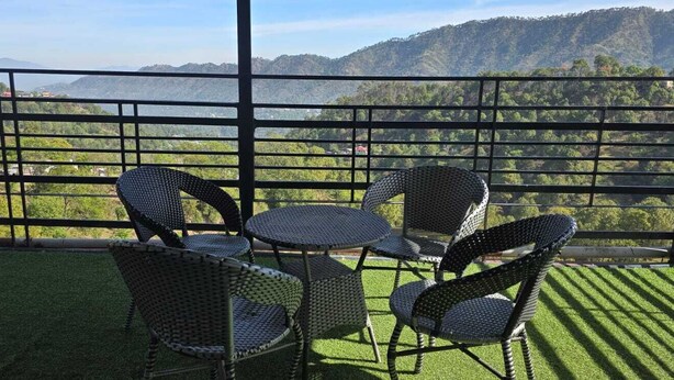 A balcony with a view of a mountainous landscape, featuring a table and chairs.