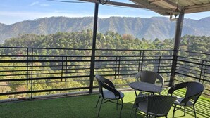 A balcony with a view of a mountainous landscape, a table, and two chairs.