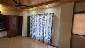 A room with a ceiling fan, wooden ceiling, a TV mounted on a wooden cabinet, a patterned curtain, and a tiled floor.