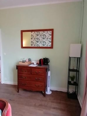 A room with a wooden dresser, a mirror with a floral frame, a white radiator, and a black shelf with a plant. - Trecastle Chambre d'Hotes (Châlus)