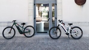 Un edificio con un cartello che recita 'CHALUS' sopra una porta, due biciclette parcheggiate davanti e un piccolo oggetto circolare appeso alla parete a destra.