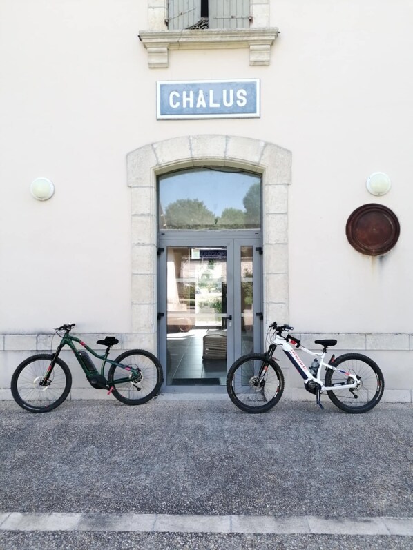 A building with a sign reading 'CHALUS' above a door, two bicycles parked in front, and a small circular object on the wall to the right. - Trecastle Chambre d'Hotes (Châlus)