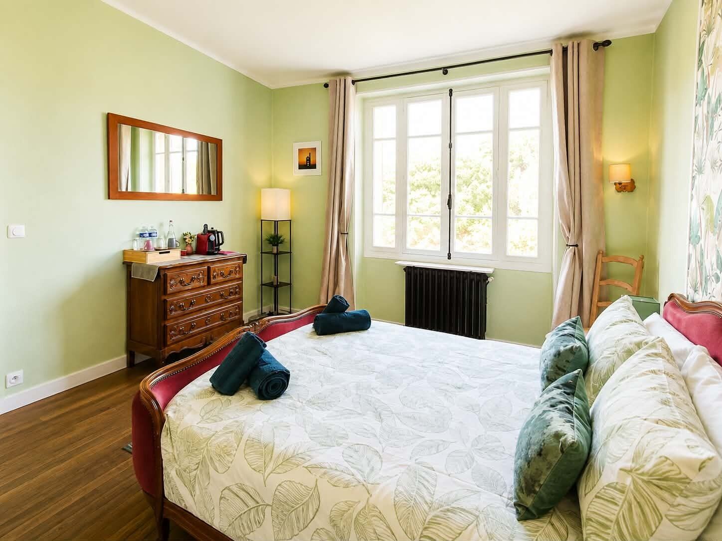 Habitación de hotel con cama, cómoda, espejo, ventana y radiador.