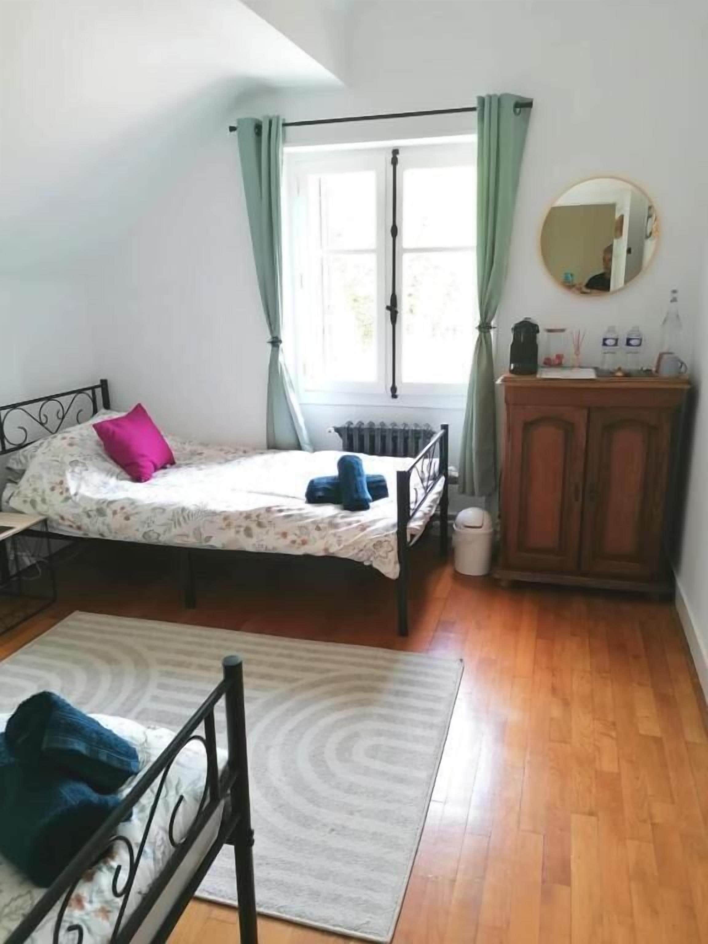 A bedroom with a bed, a dresser, a radiator, a window with curtains, and a mirror on the wall.