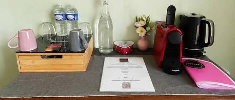 A wooden table with a tray holding mugs, bottles, and glasses, a coffee maker, a pink notebook, and a document.