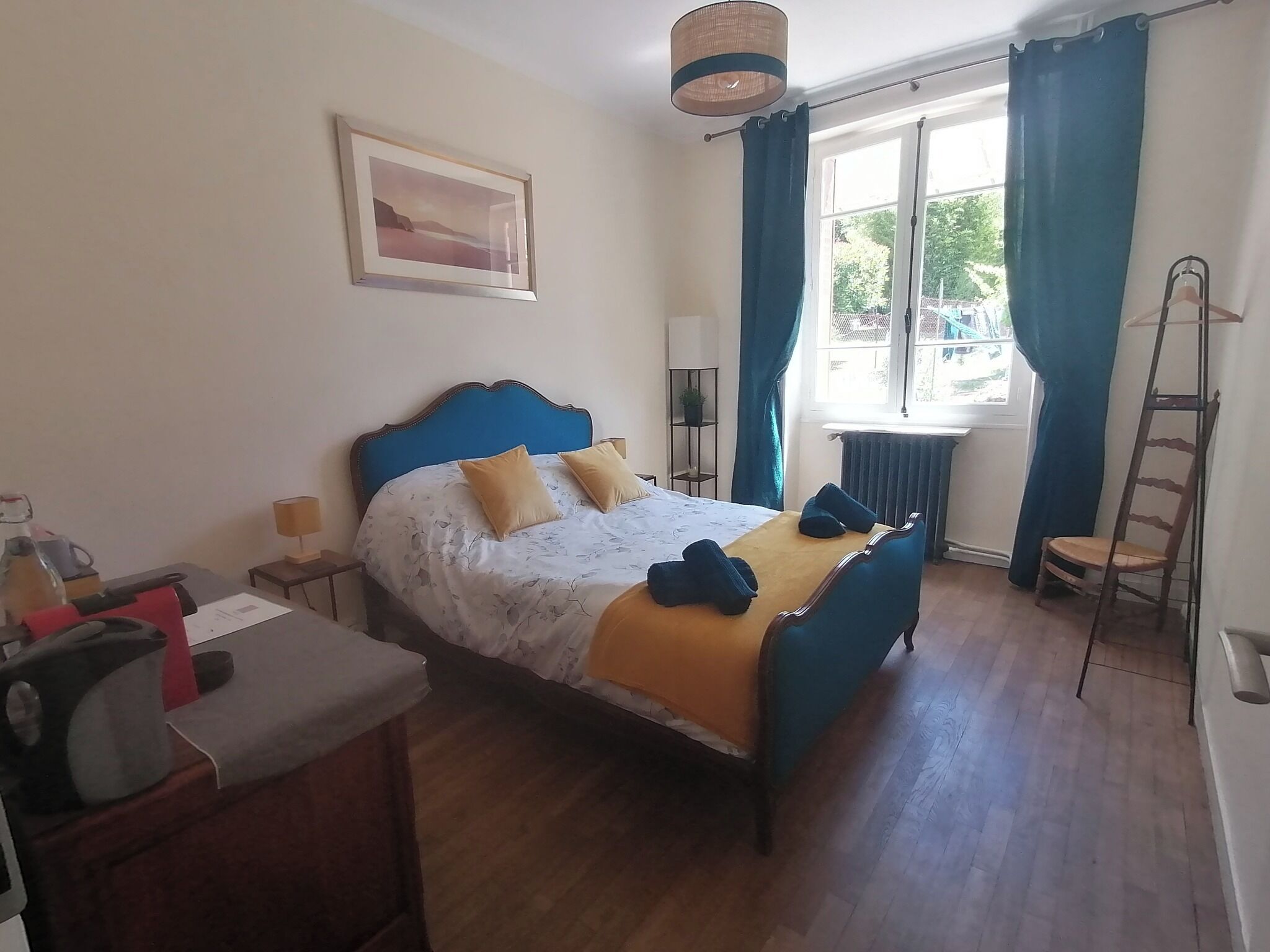 Ein Schlafzimmer mit Bett, Schreibtisch, Stuhl, einem Fenster mit Vorhängen, einer Hängelampe und einer Leiter.