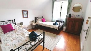 Camera da letto con due letti, un termosifone, una finestra con tende, un comodino e uno specchio.