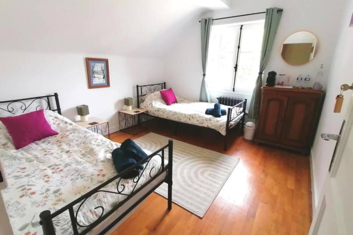 A bedroom with two beds, a radiator, a window with curtains, a bedside table, and a mirror.