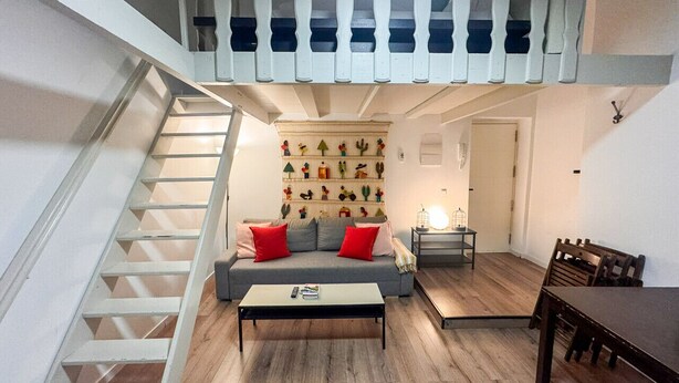 Un ambiente abitativo in stile loft con una scala, un divano con cuscini rossi, un tavolino da caffè e un tavolo da pranzo.