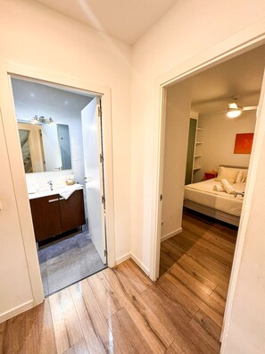 Ein schmaler Flur, der zu einem Badezimmer mit Spiegel, Waschbecken und Holzboden führt.