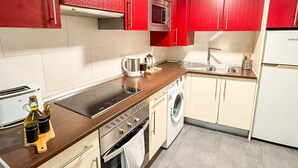Una cucina moderna con mobili rossi, forno in acciaio inossidabile, microonde integrato, lavatrice e macchina da caffè.