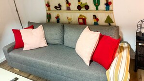 Un divano grigio con cuscini rossi e beige, un cuscino a righe e una parete con arte astratta e colorata.