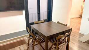 Zona pranzo con tavolo e sedie in legno, una finestra con persiane e una scala che conduce in un'altra stanza.