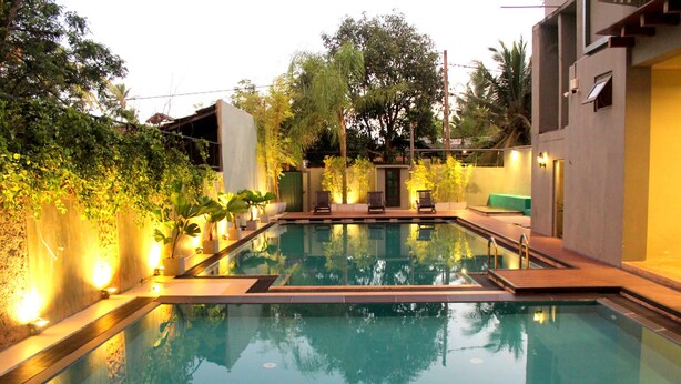 A rectangular swimming pool with a wooden deck, surrounded by potted plants and a low wall. - Morning Star Resort Pvt Ltd (Negombo)
