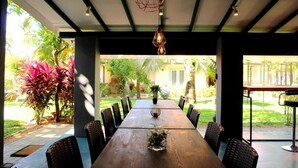 A long dining table with chairs, a hanging light fixture, and a view of a garden. - Morning Star Resort Pvt Ltd (Negombo)
