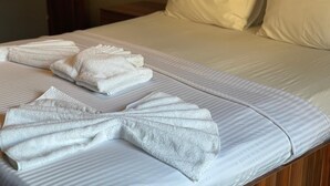 Un lit bien fait, avec des draps blancs, une serviette pliée et une couverture soigneusement repliée.