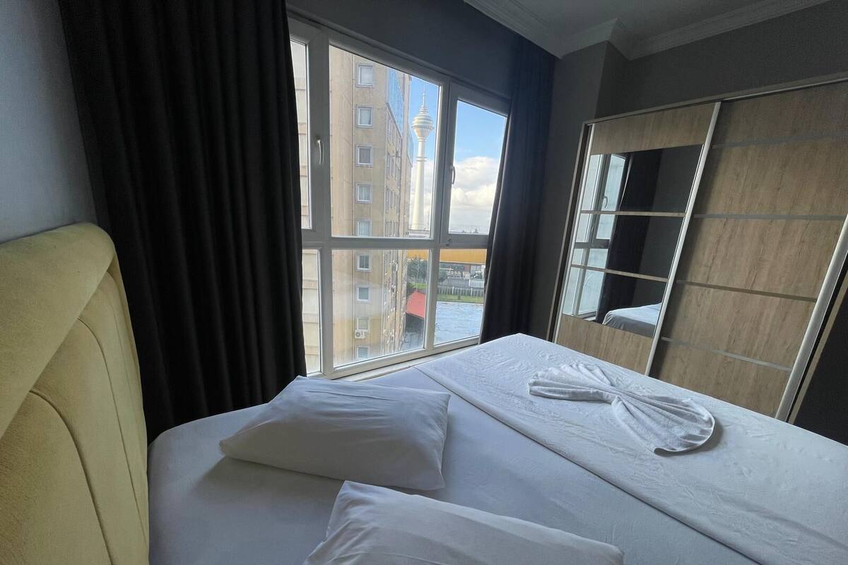 A hotel room with a bed, a large window, and a view of buildings.