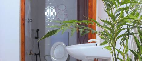 Un baño con inodoro, lavamanos, ducha y una planta pequeña.
