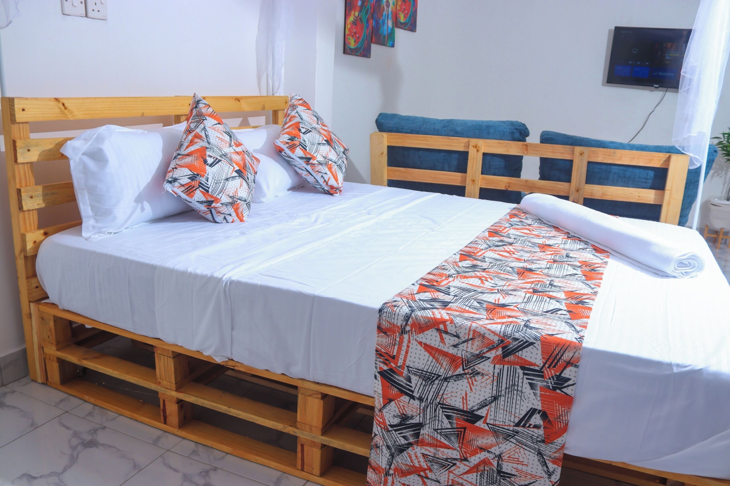 A single bed with a wooden frame, white bedding, and patterned pillows.