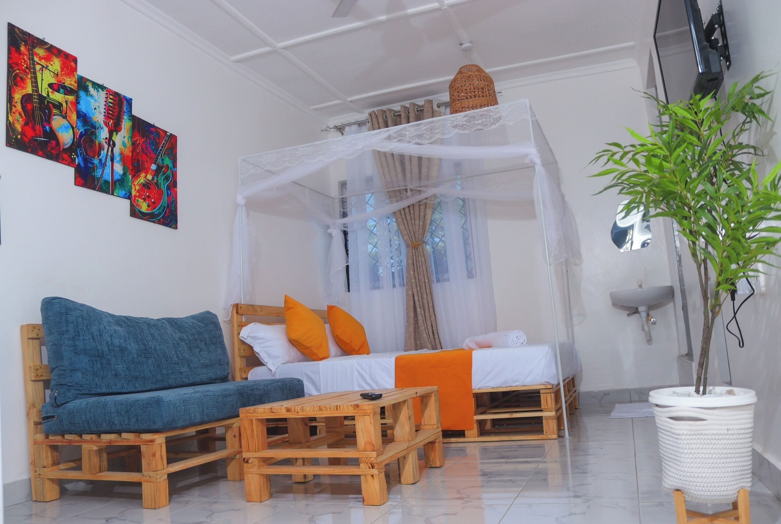 A room with a bed under a canopy, a sofa, a wooden coffee table, and a potted plant.