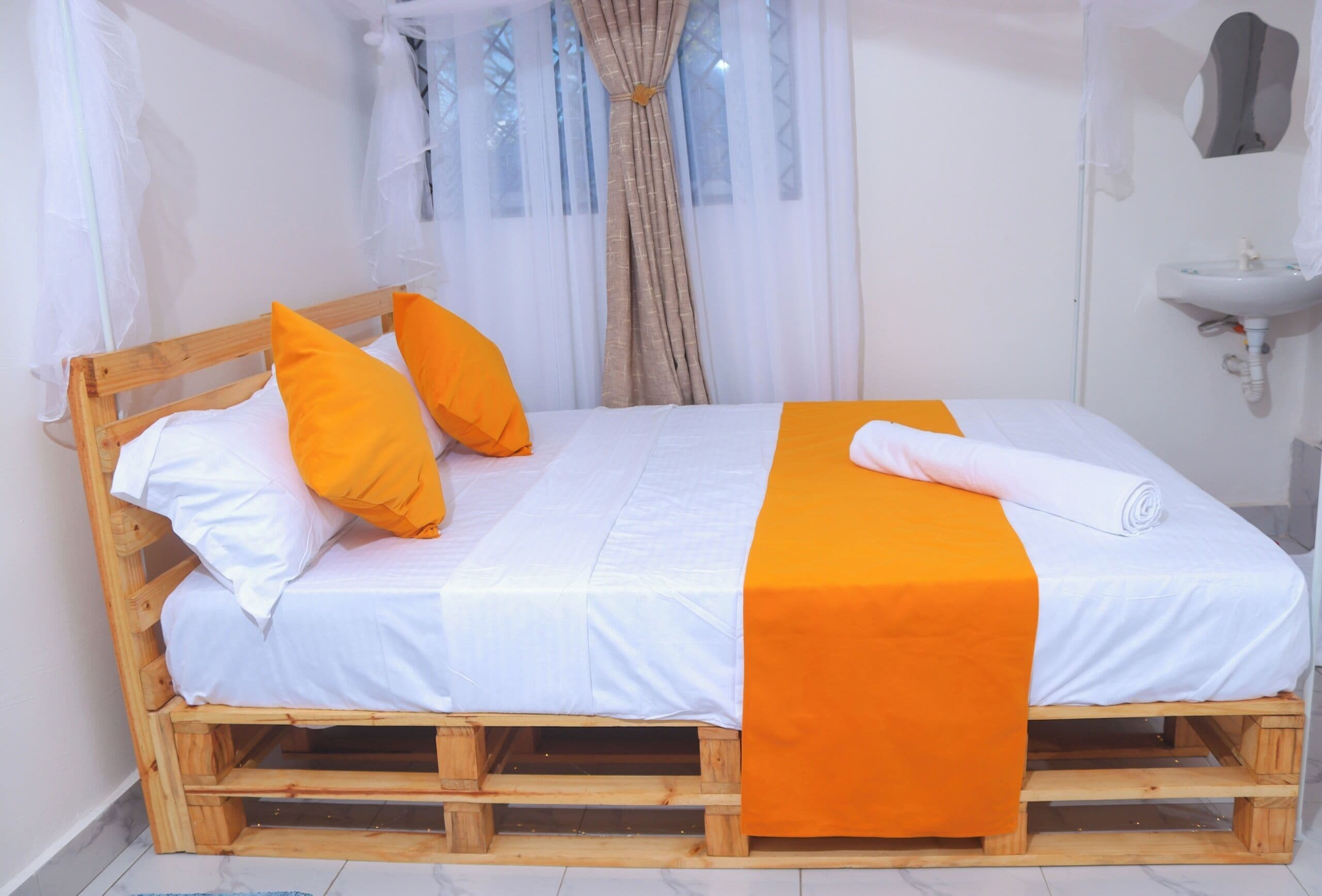 A bed with a wooden frame, white bedding, and orange accents.