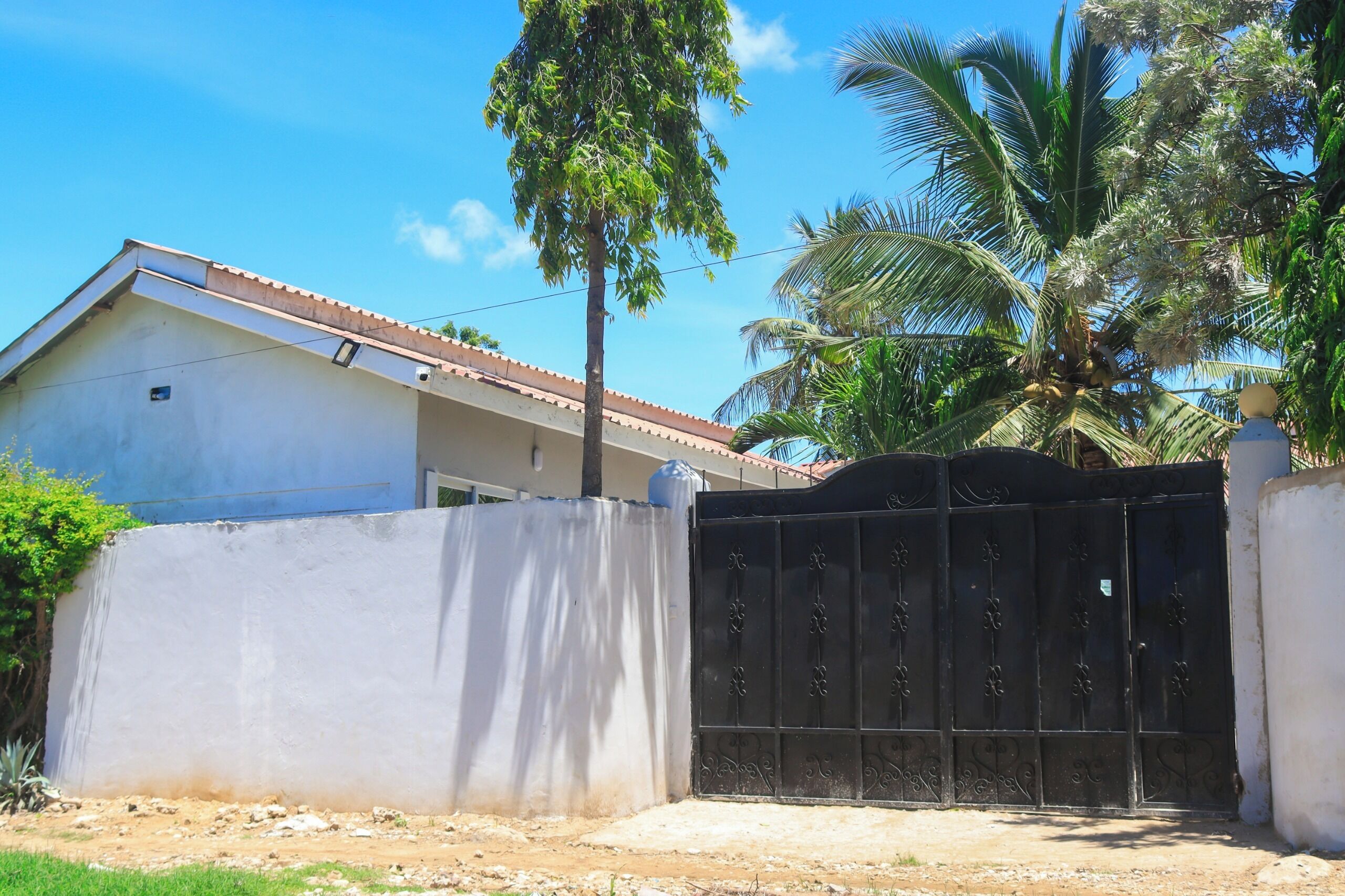 Un quartiere residenziale recintato con una casa, palme e cielo sereno.