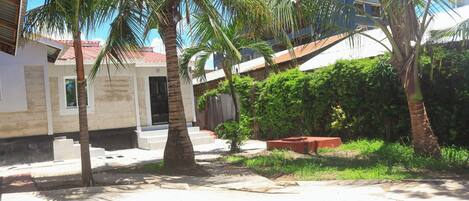 A building with a red-tiled roof, palm trees, and a paved area with steps leading to a door.