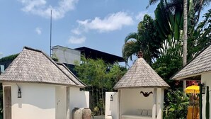 Piscina com deck ladrilhado, rodeada por pequenas construções com telhados de palha.