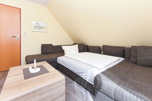 A room with a bed, a sofa, a wooden table, and a door. - Quietly located yet central apartment directly on the North Sea coast. (Esens)