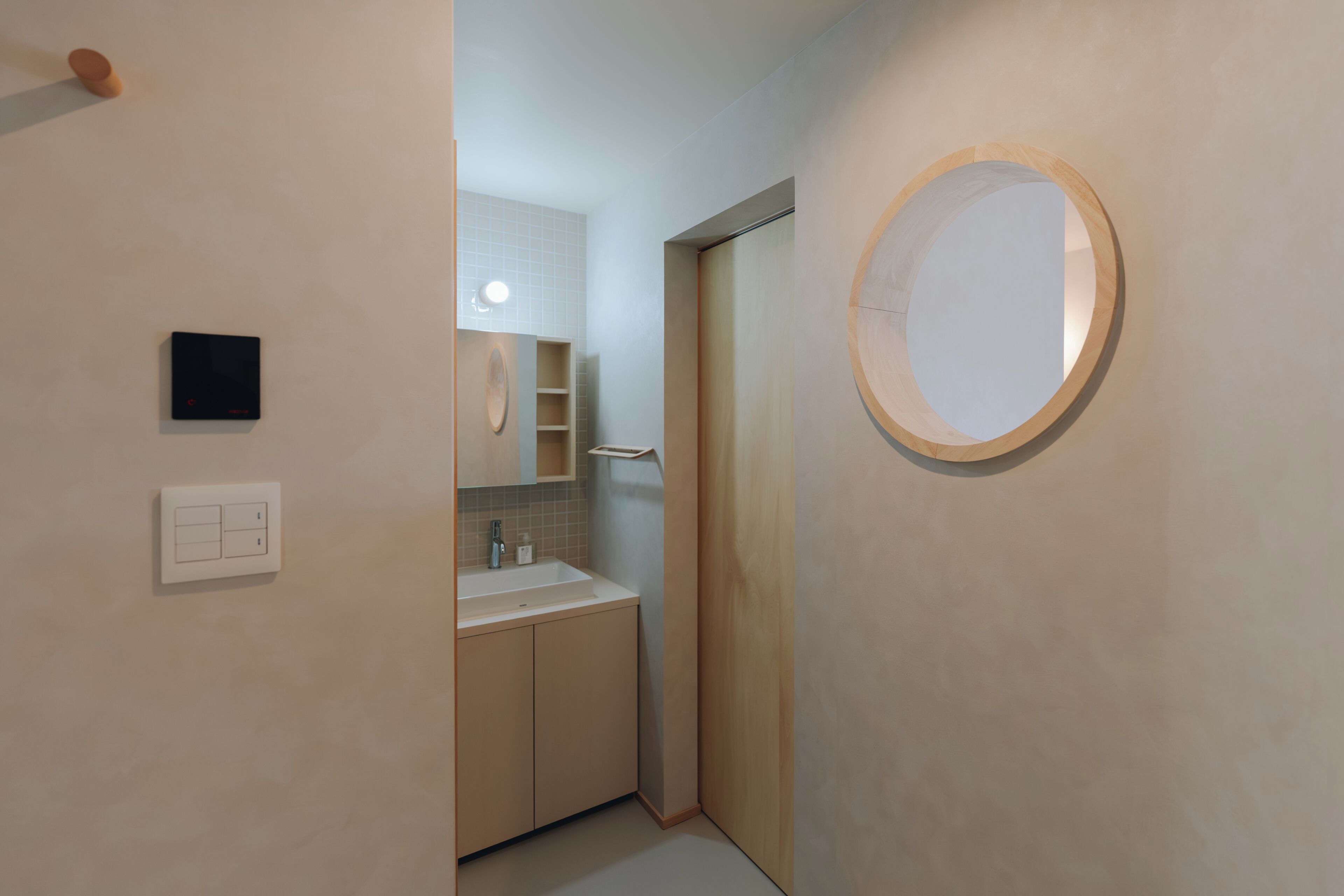 A modern bathroom with a round mirror, a sink, and a door leading to another room.