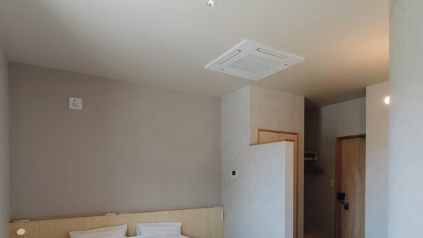 Une chambre à coucher avec un grand lit, une tête de lit en bois, une bouche d’aération au plafond et une porte donnant sur une salle de bain.