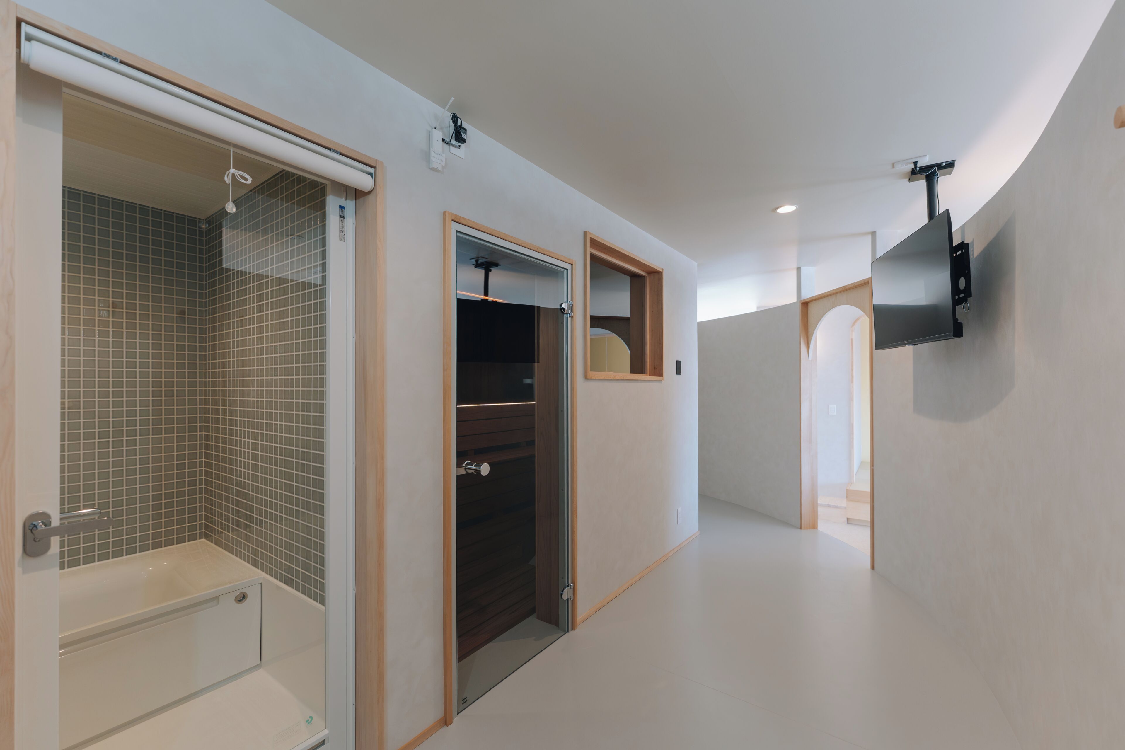 A modern bathroom with a bathtub, a shower, and a toilet. There is a TV mounted on the wall and a door leading to another room.