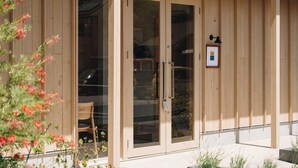 A wooden building with large glass doors, a framed picture on the wall, and a chair outside. - cuccou (Aira)