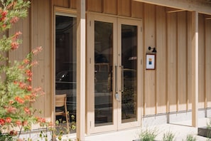 A wooden building with large glass doors, a framed picture on the wall, and a chair outside. - cuccou (Aira)