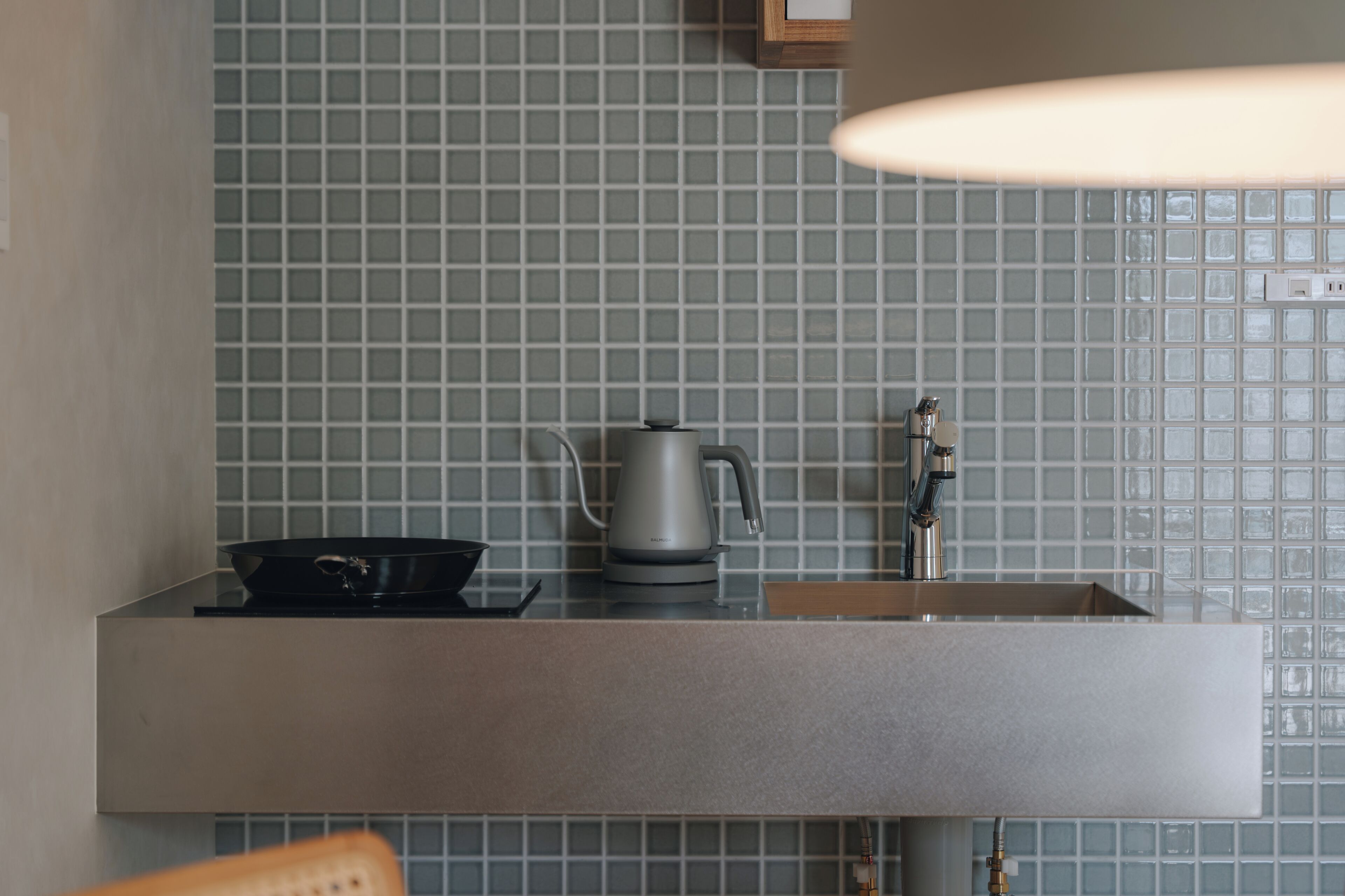 A kitchen with a modern design, featuring a stainless steel sink, a kettle, and a stove.