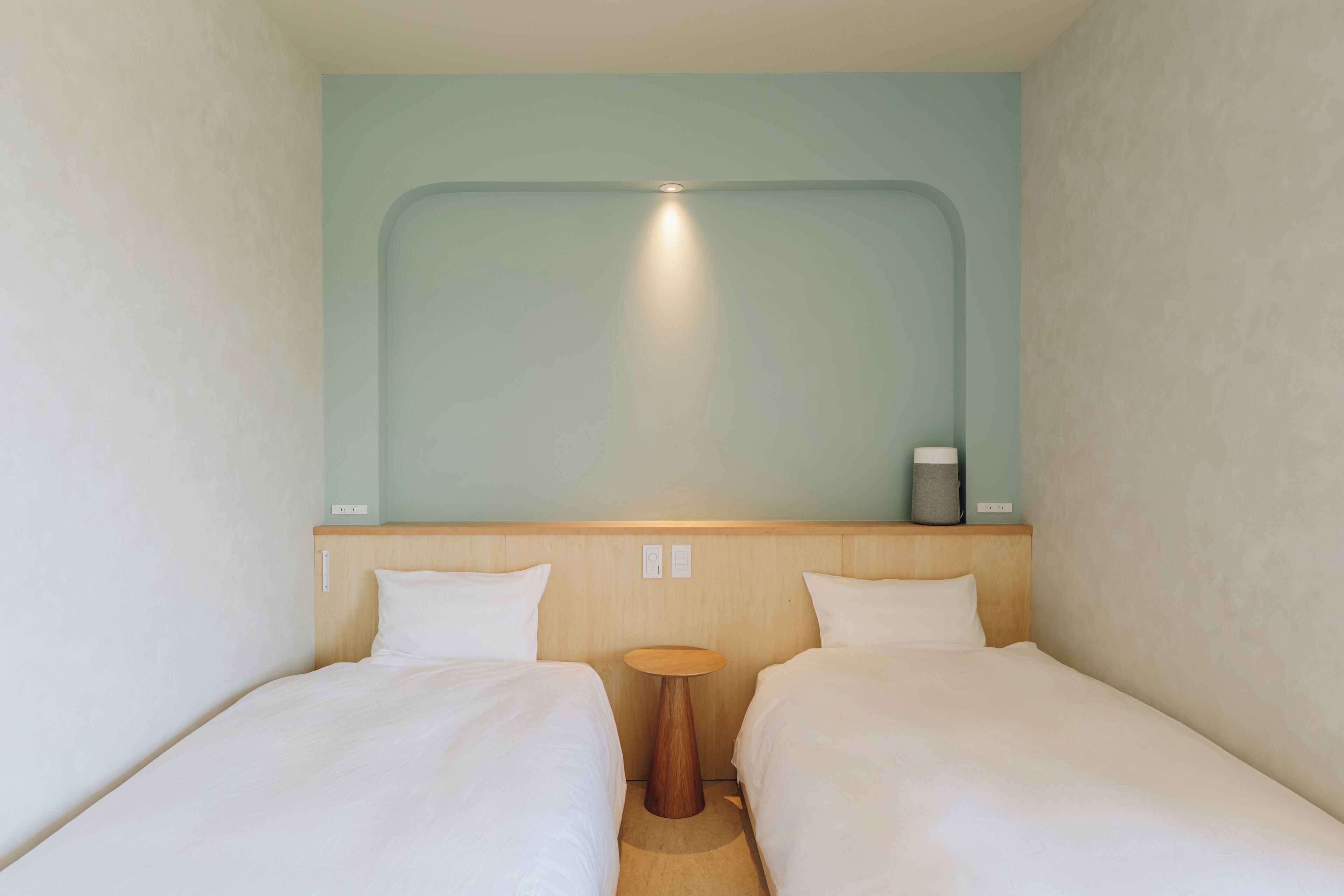 Une chambre avec deux lits simples, une petite table en bois et un luminaire fixé au mur.